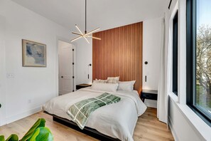 Un dormitorio moderno con una cama grande, un panel de madera decorativo, una lámpara colgante y una ventana con vistas.