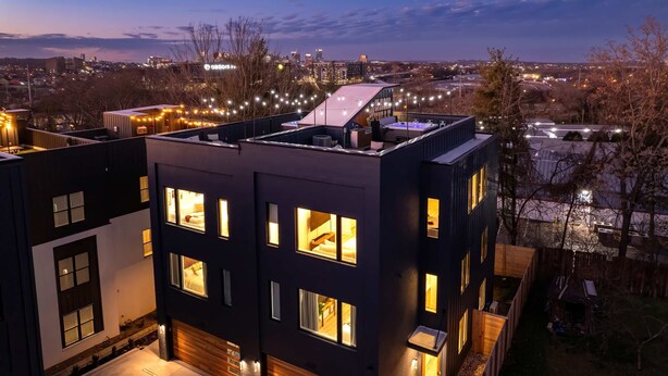 A modern multi-story building with illuminated windows and a rooftop terrace.