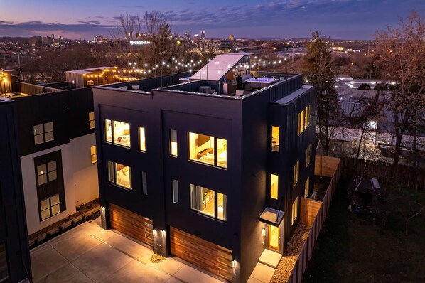 A modern multi-story building with illuminated windows and a rooftop terrace. - Nashville house with hot tub & pool table, sleeps 12 near Geodis Park (Nashville)
