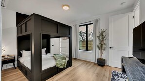A modern bedroom with a bunk bed, a desk, a potted plant, and a TV.