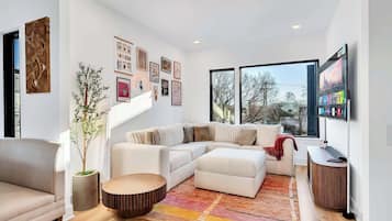A modern living room with a sectional sofa, a round coffee table, and a large window with a view of trees.