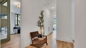 A hallway with a wooden floor, a brown leather chair, a potted plant, and a desk with a chair.