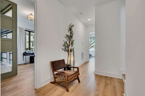 A hallway with a wooden floor, a brown leather chair, a potted plant, and a desk with a chair. - Fall getaway hot tub & game room house sleeps 12 near Geodis Park, Nashville (Nashville)