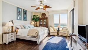 A bedroom with a large bed, a ceiling fan, a TV, a view of the ocean, and a wooden cabinet. - Breathtaking Views - 7th Floor Beachfront Condo - Tennis, Basketball, Shuffleboard, Elevator, Pool (Navarre)