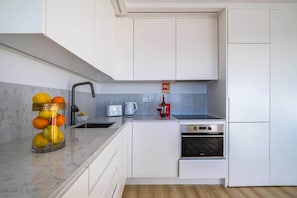 Une cuisine moderne avec des meubles blancs, un four en acier inoxydable, un grille-pain et une machine à café.