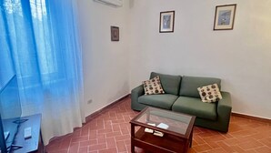 A living room with a green sofa, two pillows, a glass coffee table, and a tiled floor. - Villino Rita a Portoferraio (Portoferraio)
