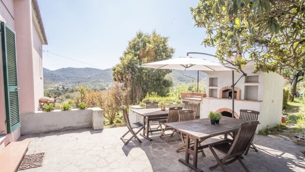 An outdoor patio with a table and chairs, a brick oven, and a view of the countryside. - Villino Rita a Portoferraio (Portoferraio)