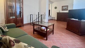 A living room with a green sofa, a wooden cabinet, a glass coffee table, and a television. - Villino Rita a Portoferraio (Portoferraio)