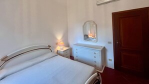 A bedroom with a bed, bedside lamp, dresser, mirror, and a chandelier. - Villino Rita a Portoferraio (Portoferraio)