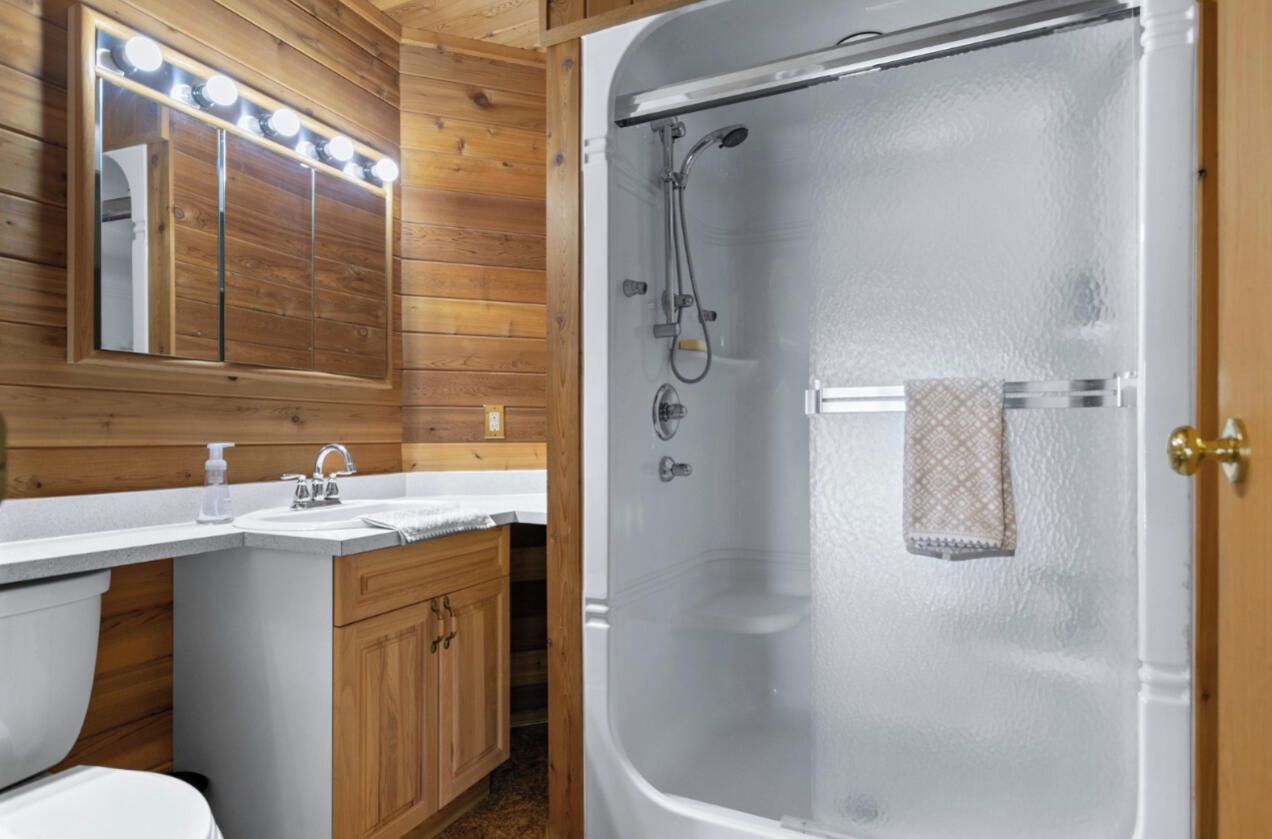 Une salle de bain avec une douche à parois de verre, un lambris en bois, un meuble-lavabo avec un miroir et un porte-serviettes.