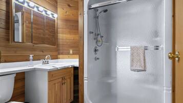 Une salle de bain avec une douche à parois de verre, un lambris en bois, un meuble-lavabo avec un miroir et un porte-serviettes.