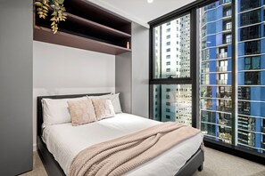 Een moderne slaapkamer met een groot bed, inbouwkasten en uitzicht op een stadslandschap door een groot raam.