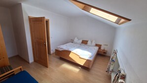 Un dormitorio con una cama de madera, una mesita de noche, una silla azul y un techo inclinado con tragaluces.
