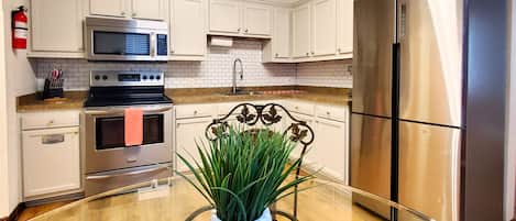 Una cocina moderna con armarios blancos, electrodomésticos de acero inoxidable y una mesa de comedor de vidrio con una planta en maceta.