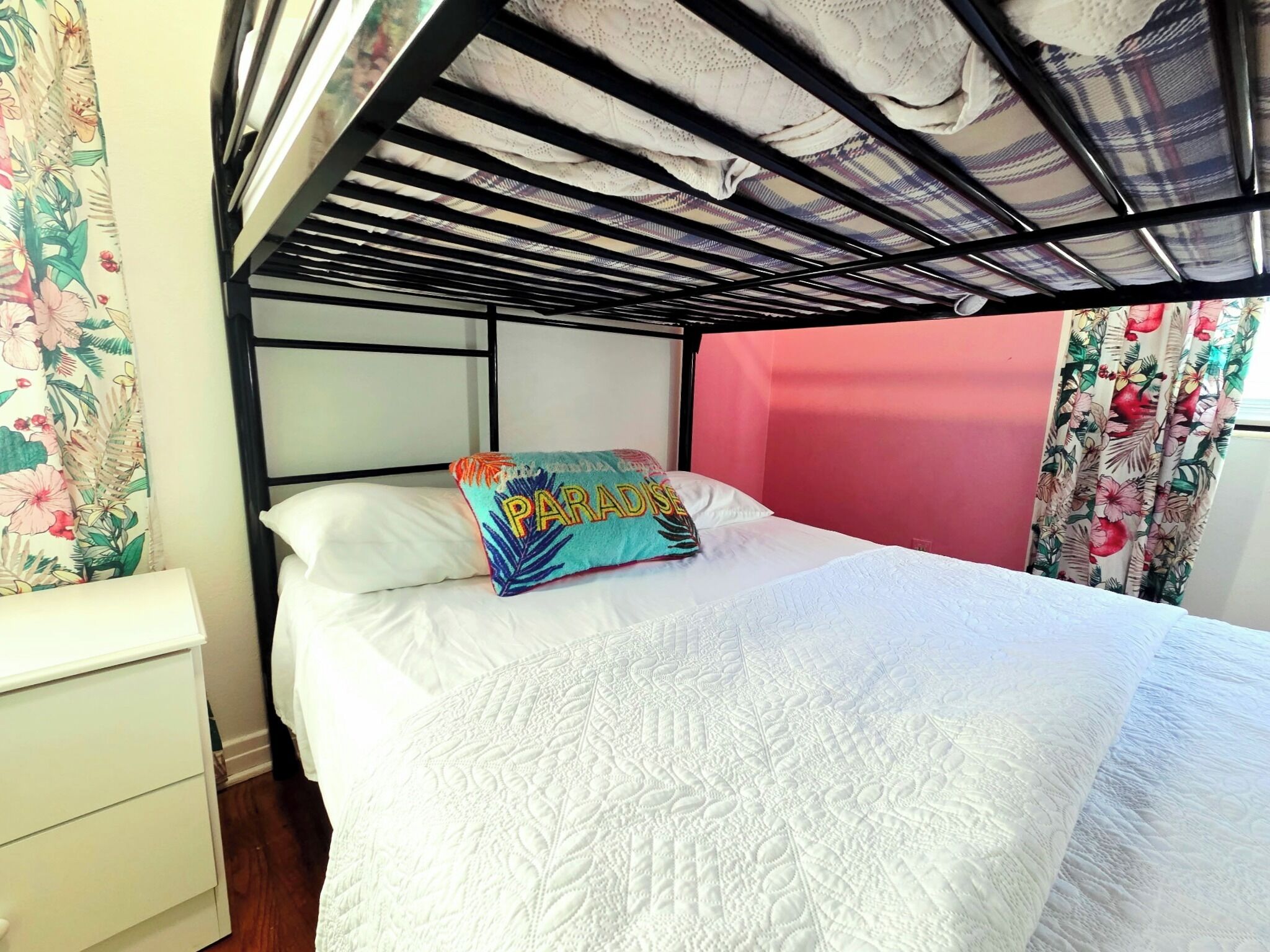 Una cama litera con cabecera blanca, un cojín colorido y cortinas con estampado floral.