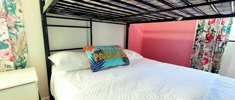 Una cama litera con cabecera blanca, un cojín colorido y cortinas con estampado floral.