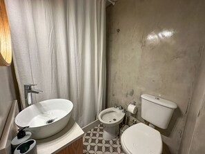 A bathroom with a large vessel sink, a bidet, a toilet, and a shower curtain.