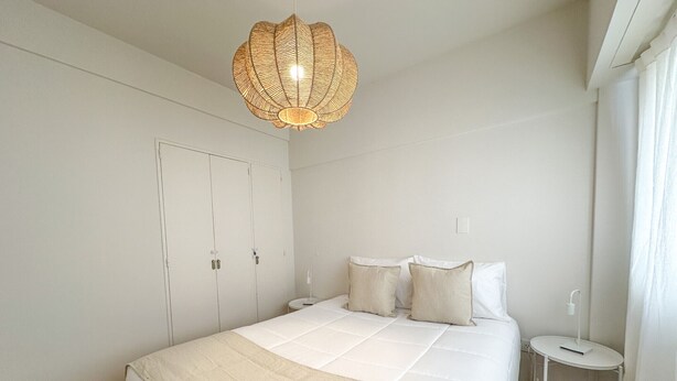 A bedroom with a bed, bedside table, lamp, wardrobe, and a hanging light fixture. - Modern apartment in Recoleta near Recoleta Mall (Buenos Aires)