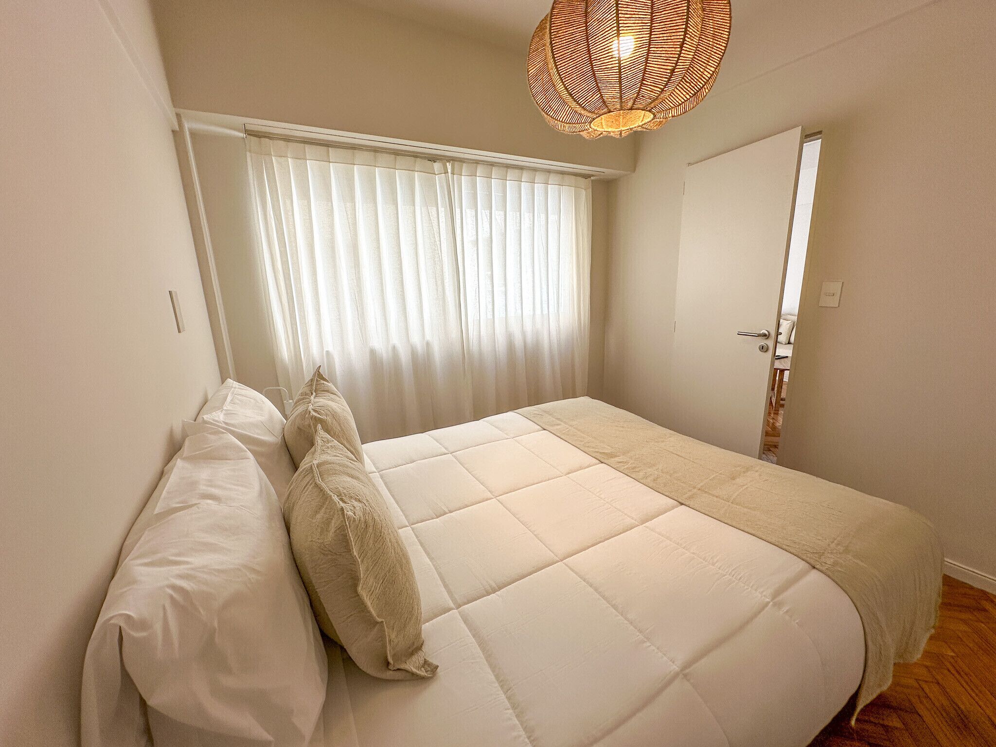 Un dormitorio con cama, cortinas blancas, una puerta y una lámpara de fibra.