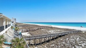 Blick auf einen Strand mit einer Holzpromenade, die zum Ufer führt, einer Flagge und einem Gebäude mit Balkon.