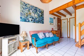 Un salon avec un canapé, un téléviseur, un tableau et un escalier.