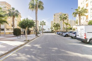 A street lined with palm trees and parked cars, with buildings on either side.