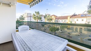 A balcony with a table and chairs, overlooking a residential area with buildings and palm trees.