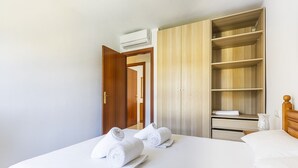 A hotel room with a bed, two rolled towels, a wardrobe, and a small table with a vase.