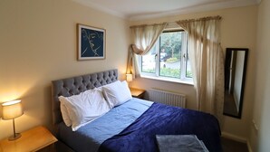 Een slaapkamer met een bed, een bedlampje, een raam met gordijnen en een lijst met een foto aan de muur.