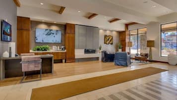 A modern lobby with a reception desk, seating area, and large windows.