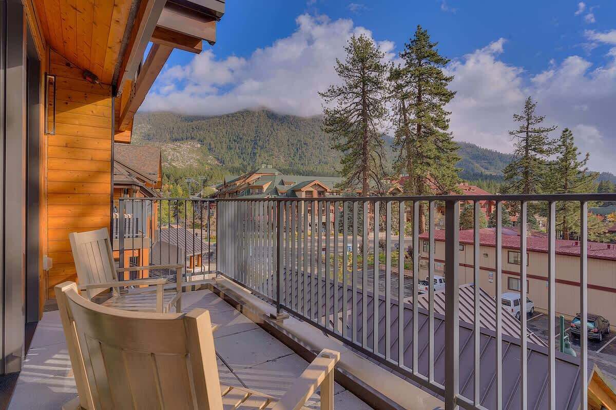 Un balcon en bois avec des chaises, une vue sur une montagne et un espace de stationnement.