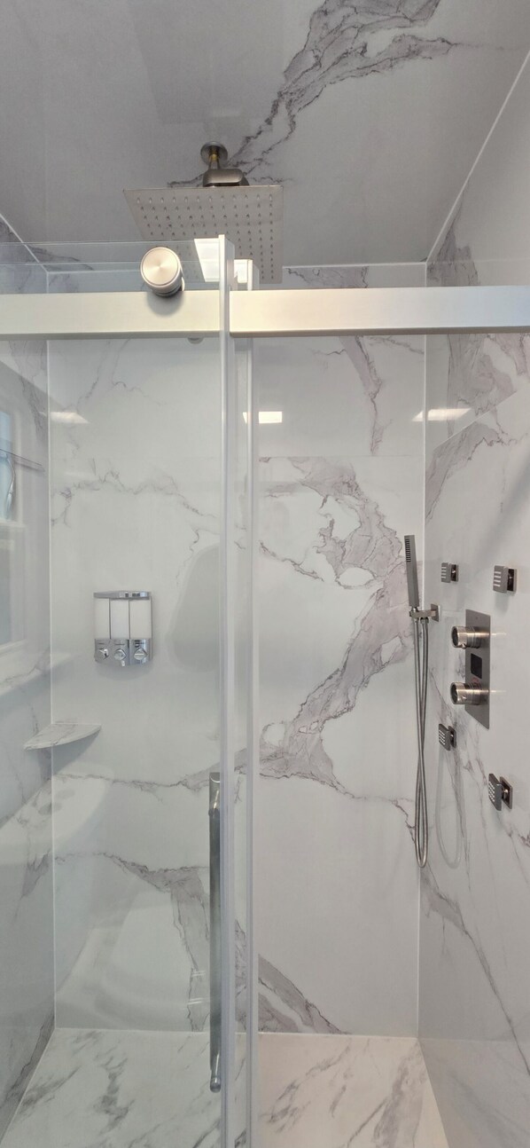 A modern bathroom with a glass shower enclosure, marble walls, and a ceiling-mounted showerhead. - Private Entrance, King Sze Bed,Luxurious Shower (Vallejo)