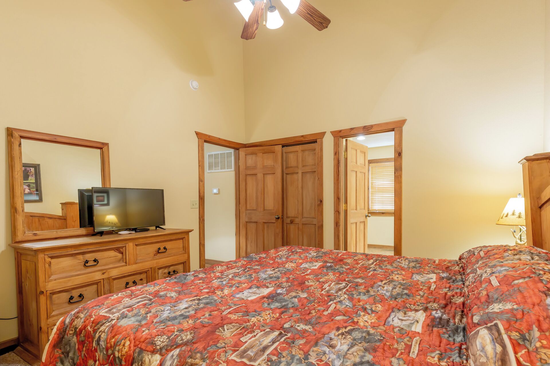 A bedroom with a large bed, a wooden dresser, a television, and a ceiling fan.