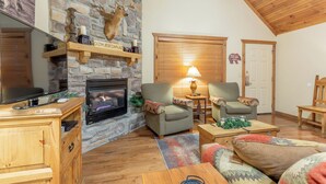 Un salon chaleureux avec une cheminée en pierre, un plafond en bois et des sièges confortables.