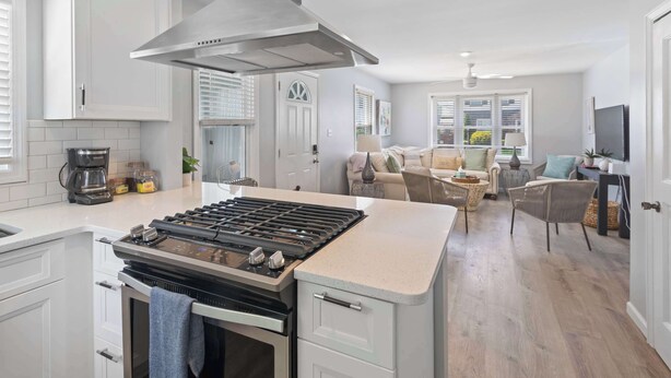 Cocina moderna con una isla central, armarios blancos y una campana extractora de acero inoxidable.