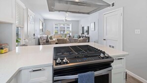 Una cocina moderna con una isla central, extractor de acero inoxidable y vistas a un área de estar con sofá y sillones.