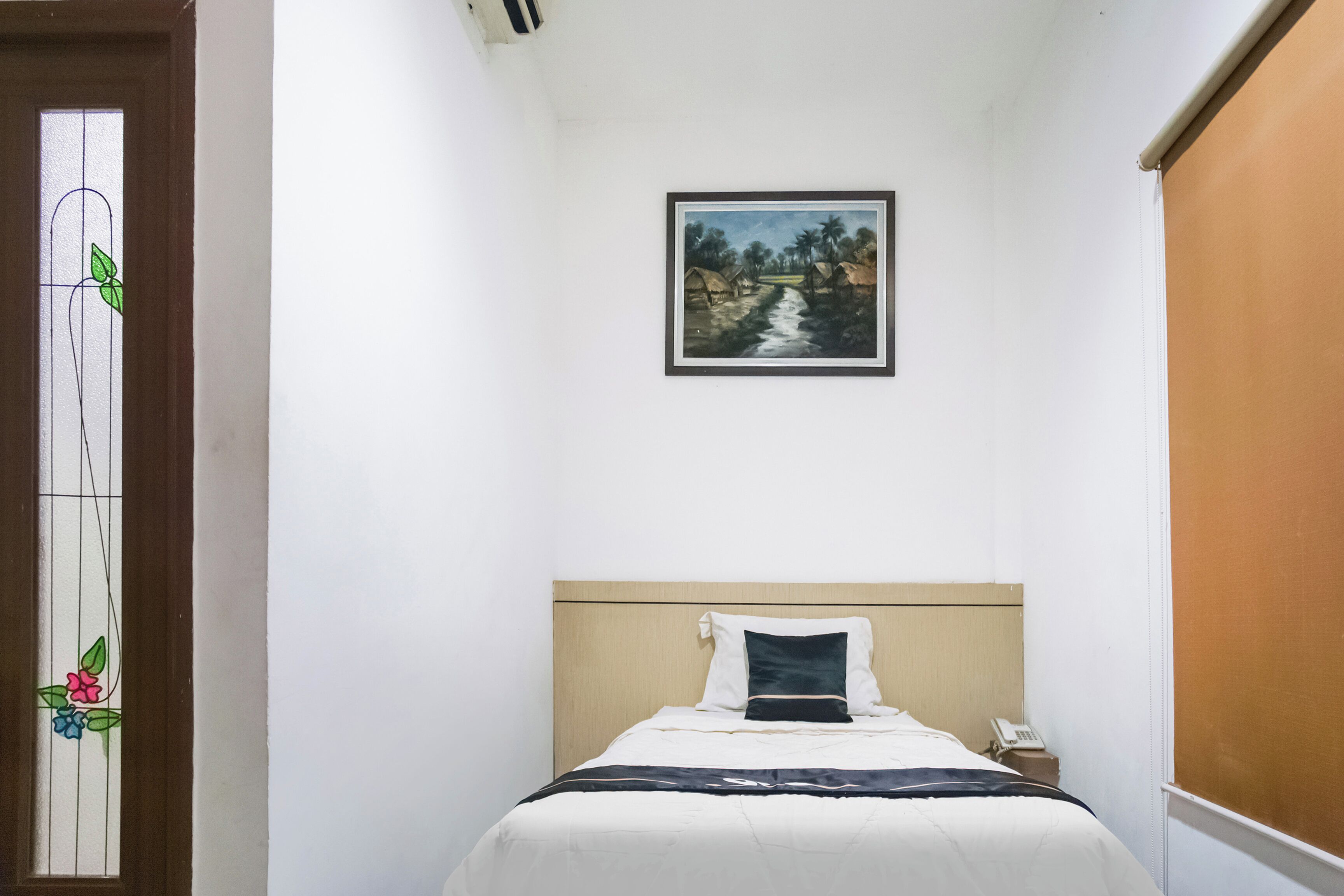 A bedroom with a bed, a nightstand, a framed picture on the wall, and a window with a floral design.