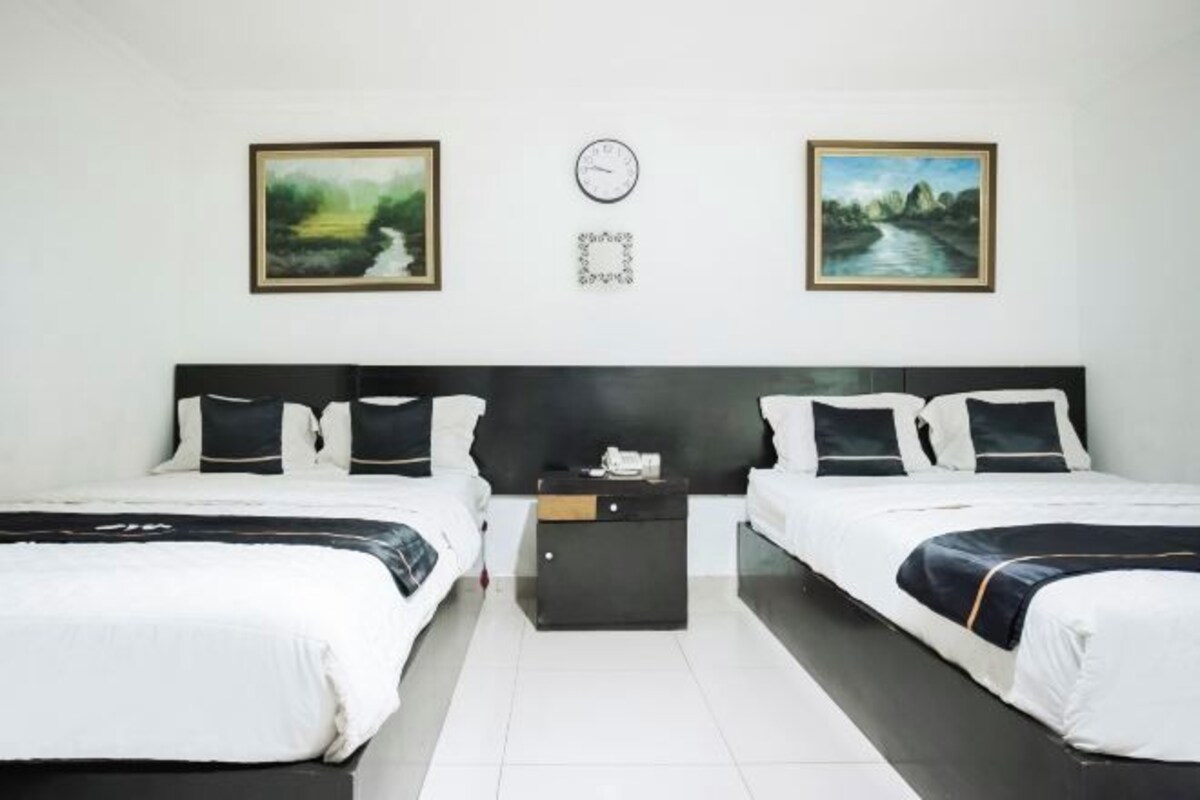 A hotel room with two beds, a nightstand, a clock, and two framed pictures on the wall.