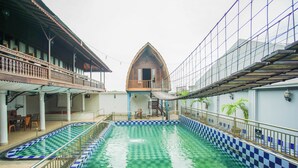 Une piscine à motifs en damier, un bâtiment en bois doté d’un balcon et une allée couverte.