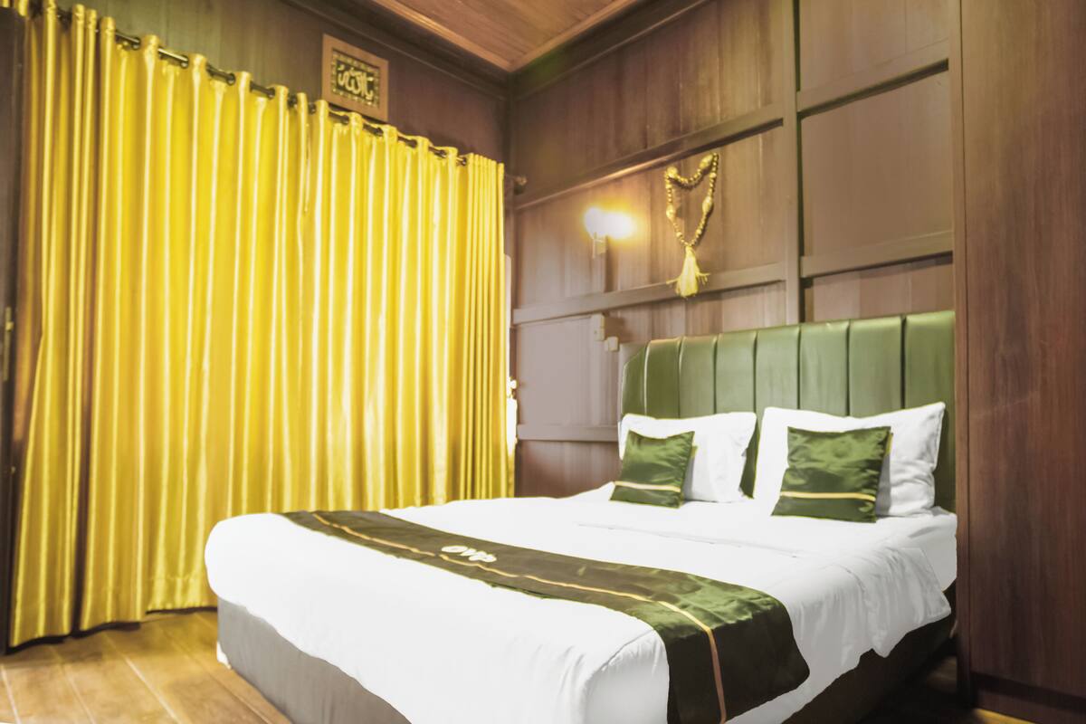 A hotel room with a large bed, green and white bedding, wooden paneling, and a yellow curtain.