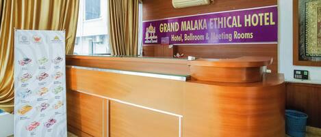 A reception desk at Grand Malaka Ethical Hotel with a sign indicating hotel, ballroom, and meeting rooms.