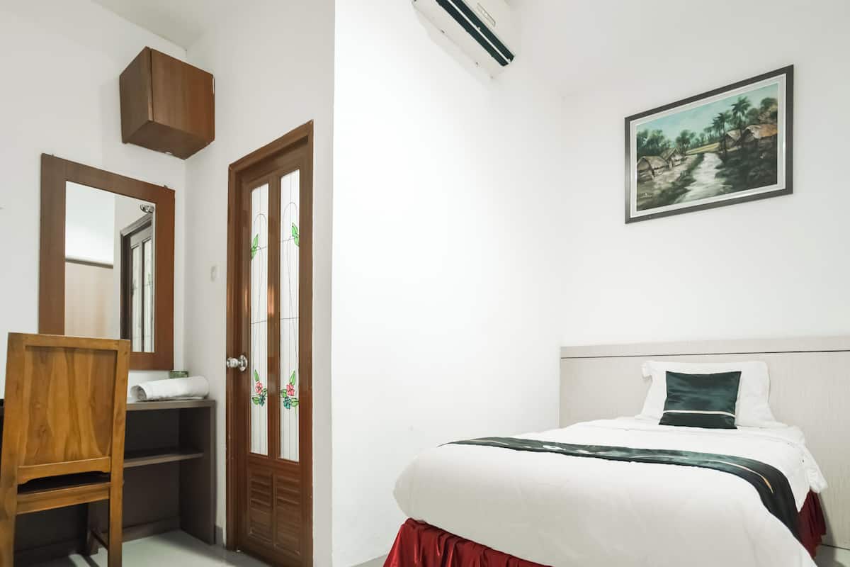 A bedroom with a bed, a chair, a wooden wardrobe, a door with glass panels, and a wall-mounted air conditioner.