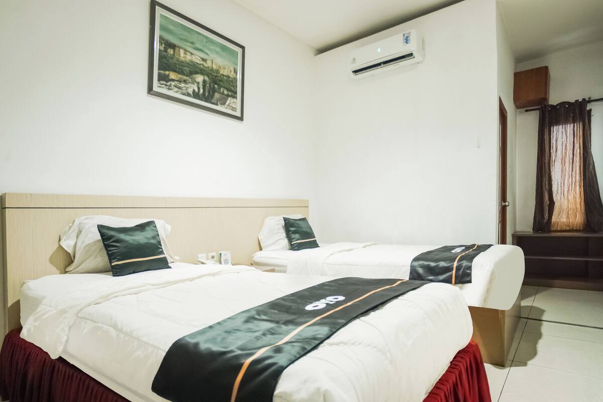A hotel room with two beds, a framed picture on the wall, and an air conditioning unit.