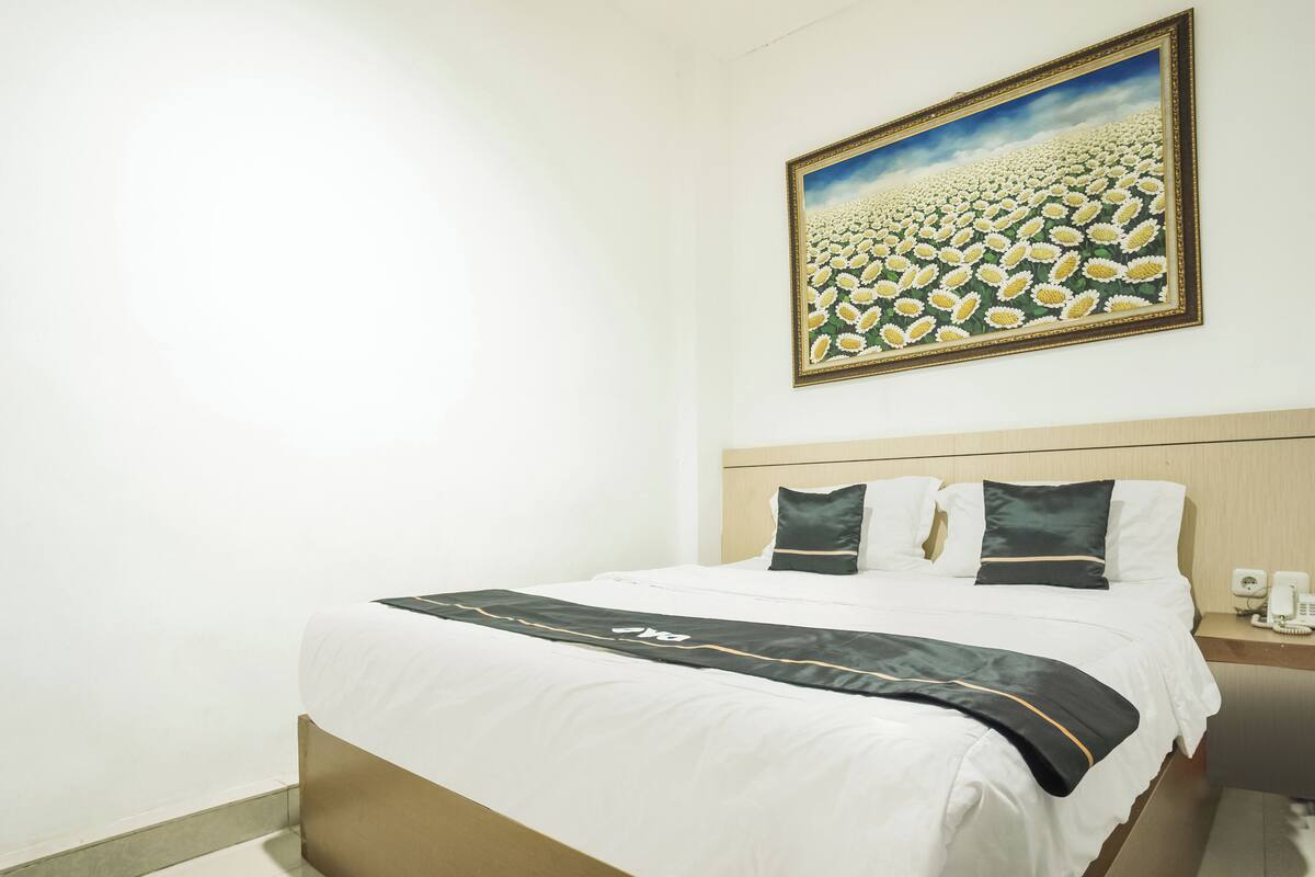A hotel room with a bed, a headboard, a nightstand with a phone, and a painting of a field of flowers on the wall.