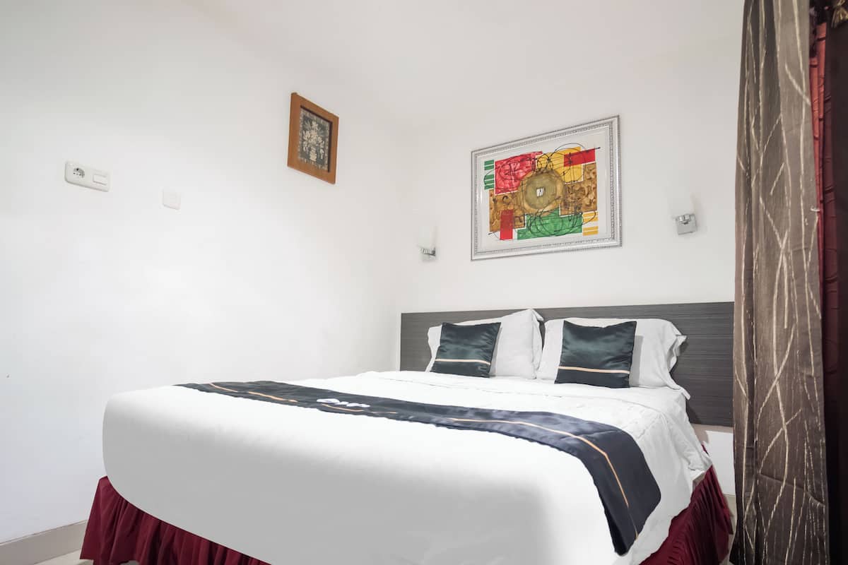 A neatly made bed with a white and dark-colored bedspread, two pillows, and a headboard. There is a framed picture on the wall above the bed.