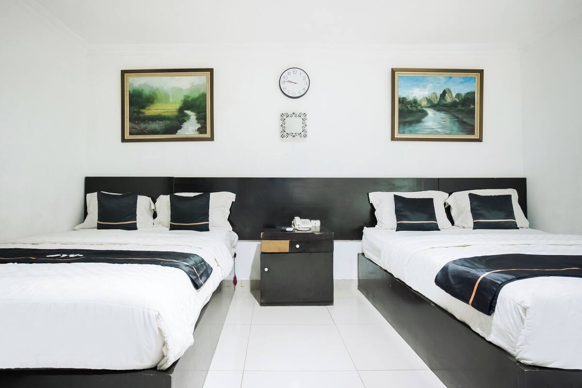 A hotel room with two beds, a nightstand, a clock, and two framed pictures on the wall.
