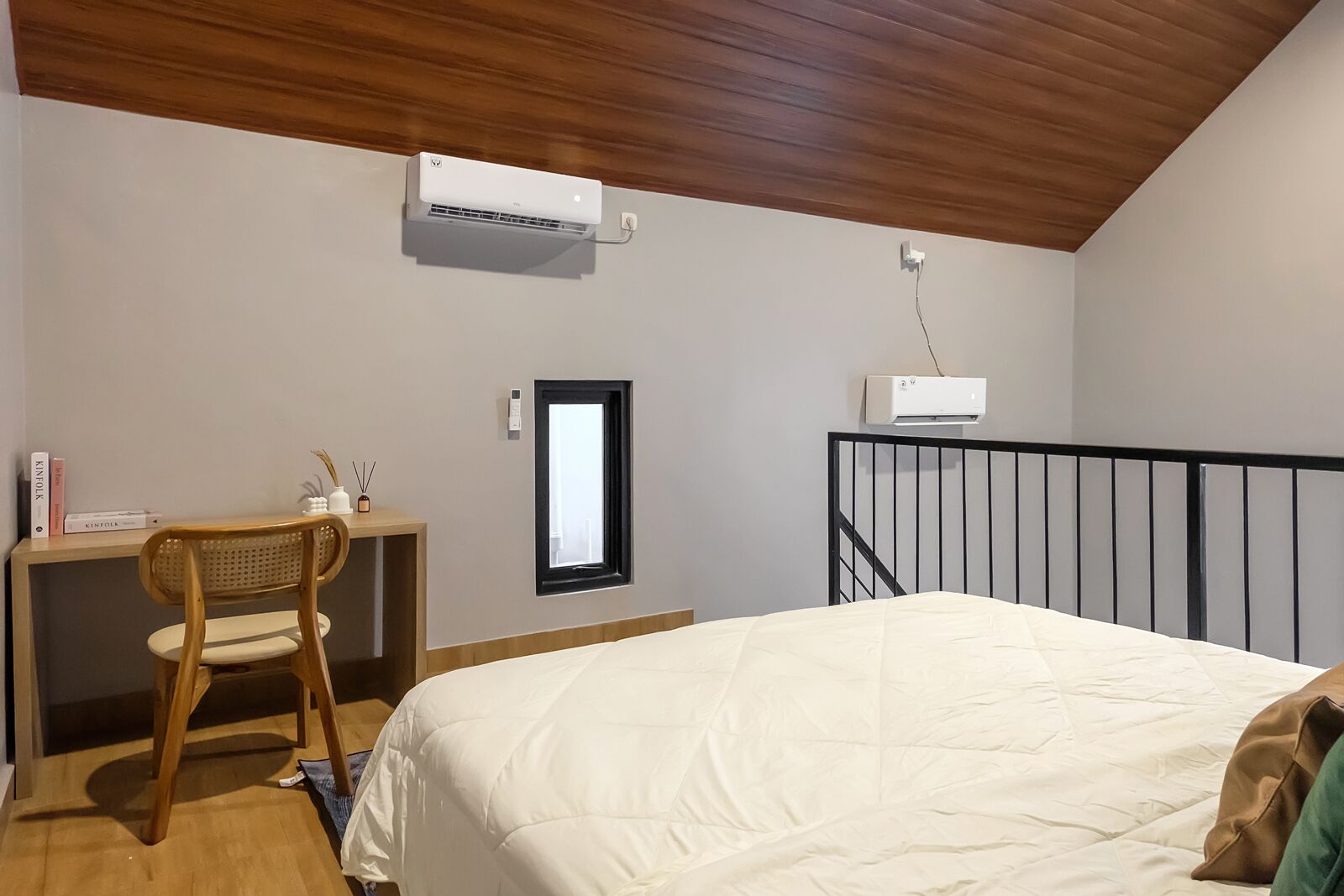 A bedroom with a bed, a desk with a chair, an air conditioning unit, and a window.