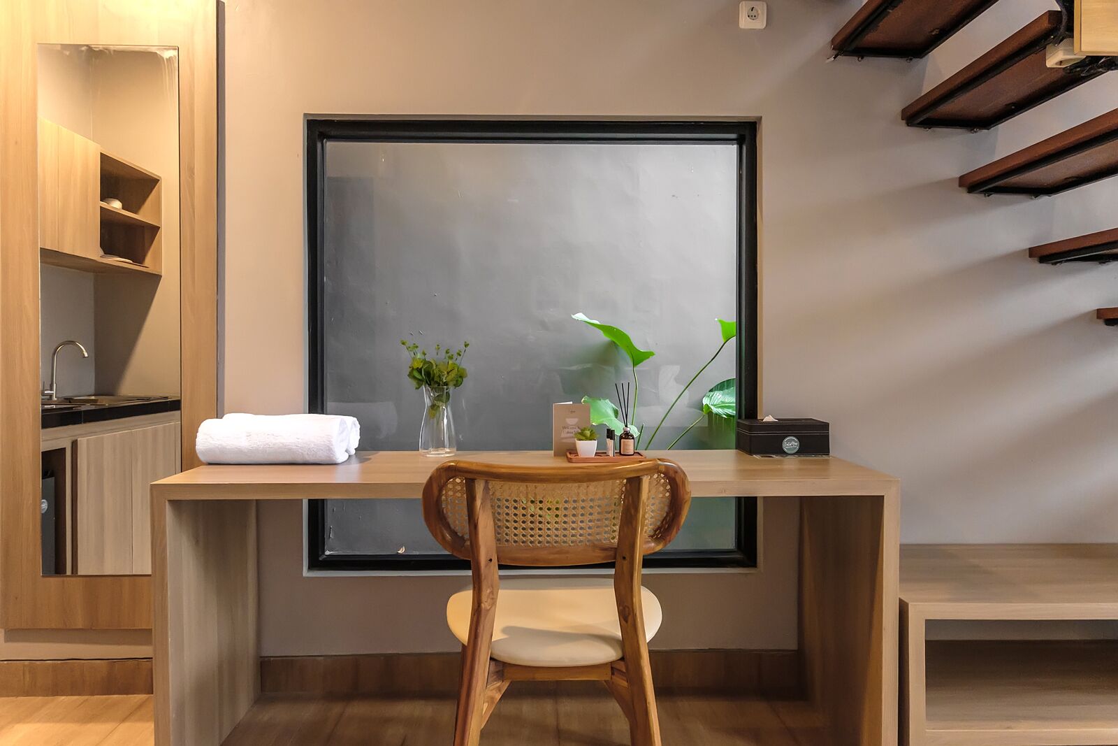 A modern room with a large window, a wooden desk, a chair, and a small plant on the desk.