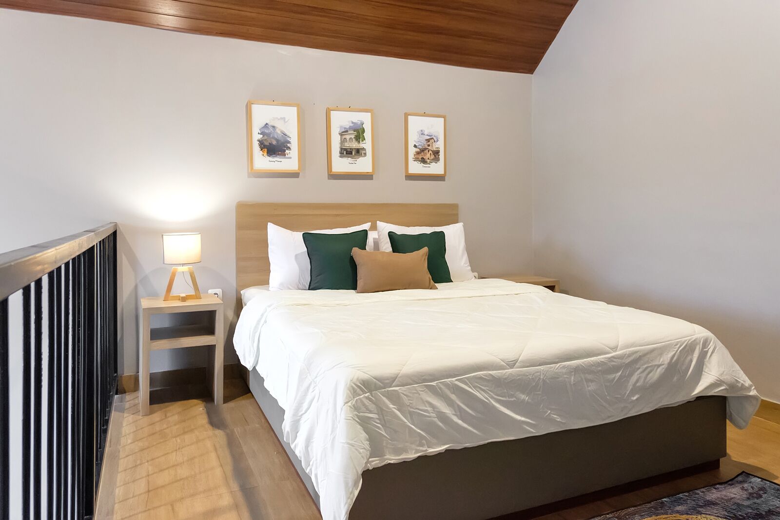 Un dormitorio con una cama grande, una mesita de noche con lámpara y tres cuadros en la pared.