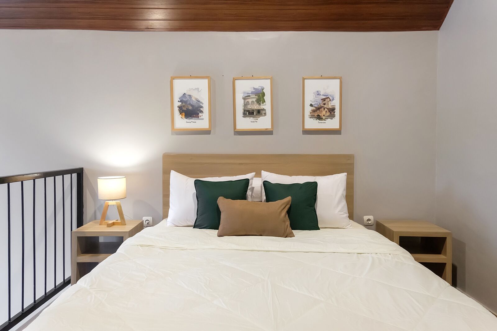 A neatly made bed with white and green pillows, a wooden headboard, and three framed pictures on the wall above.